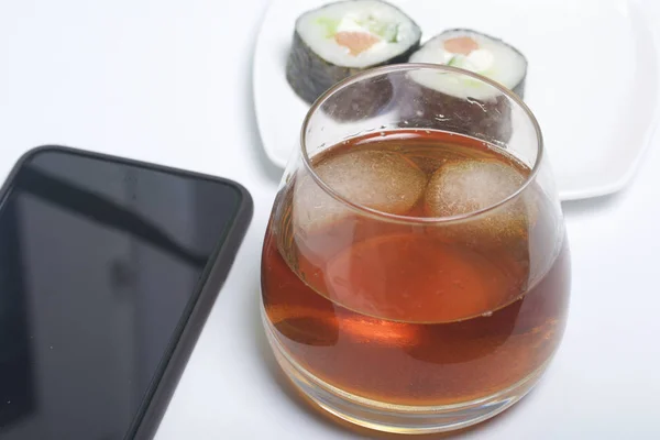 Whisky mit Eis im Glas und Sushi. In der Nähe befindet sich ein Smartphone. Rest des Tages frei. — Stockfoto