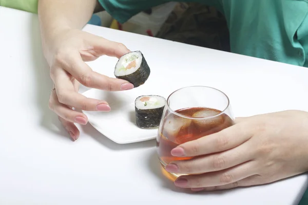 Девушка берет стакан виски со стола со льдом. Другая рука берет с тарелки суши. Остаток выходного дня . — стоковое фото