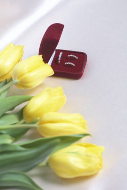 Sevdikleriniz için hediyeler. Bir buket Sarı laleler ışık bir yüzeye dağınık olduğunu. Yakınlarda bir açık kadife kırmızı renk altın süslemeli kutun.