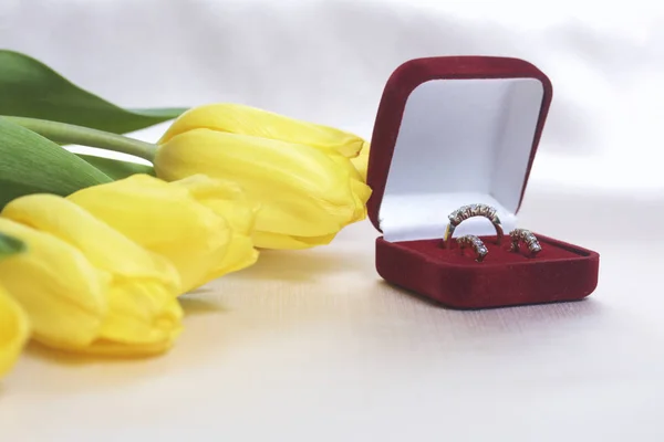 Dárky pro blízké. Kytice žlutých tulipánů je rozptýlena na lehké povrchu. Nedaleko je otevřený velvet box červené barvy s zlaté ornamenty. — Stock fotografie