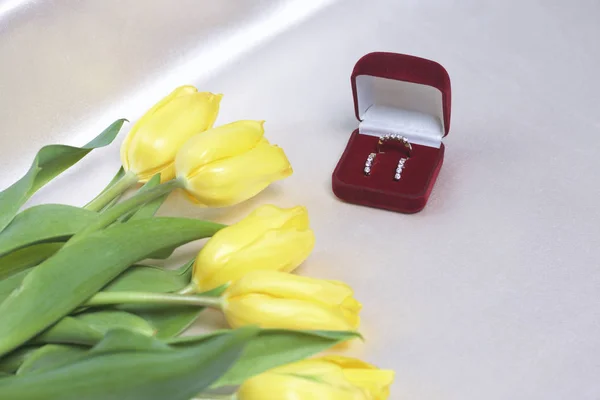 Presentes para entes queridos. Um buquê de tulipas amarelas é espalhado em uma superfície leve. Nas proximidades é uma caixa de veludo aberto de cor vermelha com ornamentos de ouro . — Fotografia de Stock