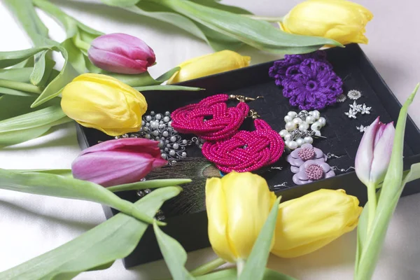Regalos para seres queridos. Un ramo de tulipanes amarillos y rosados está esparcido sobre una superficie clara. A continuación un conjunto de pendientes en una caja . — Foto de Stock