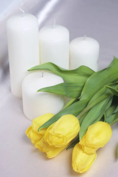 Kytice žlutých tulipánů je rozptýlena na lehké povrchu. Nedaleko jsou dekorativní svíčky. Detail, pohled shora. — Stock fotografie