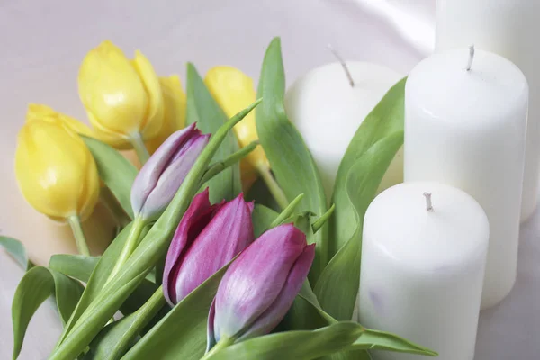 Um buquê de tulipas amarelas e rosa é espalhado em uma superfície leve. Nas proximidades estão velas decorativas. Close-up, vista superior . — Fotografia de Stock