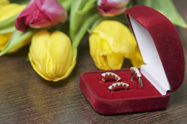 Presentes para entes queridos. Um buquê de tulipas amarelas e rosa é espalhado em uma superfície escura. Nas proximidades é uma caixa de veludo aberta de cor vermelha com jóias de ouro . — Fotografia de Stock