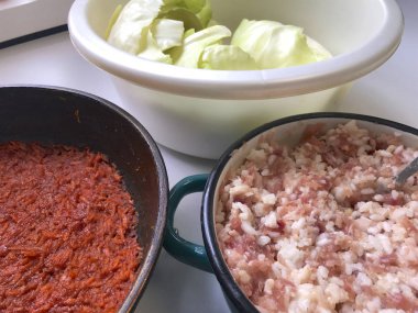 Masaya lahana rulo pişirme için unsurlarıdır. Kahvaltılık havuç bir tavada kıyma bir konteyner ve lahana bir havzasında kalkıyor..