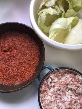 Masaya lahana rulo pişirme için unsurlarıdır. Kahvaltılık havuç bir tavada kıyma bir konteyner ve lahana bir havzasında kalkıyor..