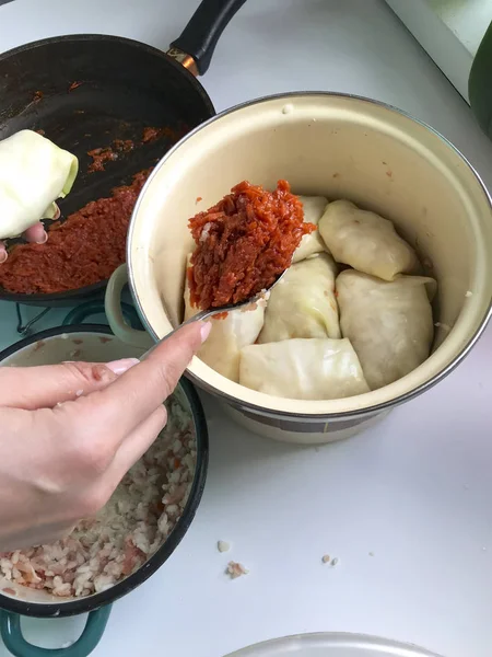 La mujer vierte las capas de rollos de col en una cacerola con zanahorias dispersas. Zanahorias infladas en una sartén, carne picada en un recipiente y hojas de col en un recipiente . — Foto de Stock