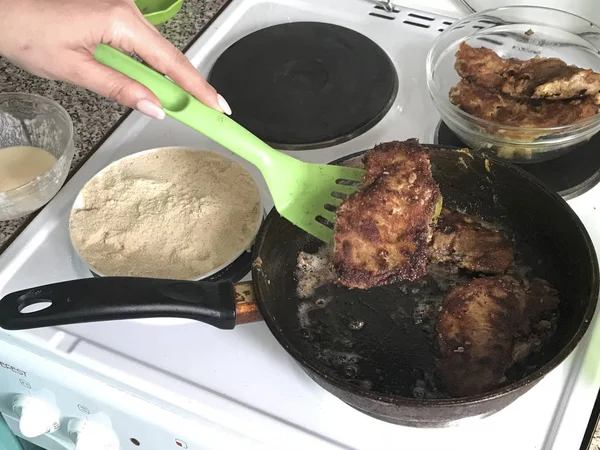 Una mujer toma una chuleta preparada de la sartén. Los trozos de carne se fríen en una sartén caliente. Hay salpicaduras de grasa caliente . — Foto de Stock