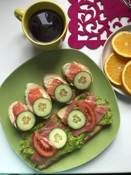 Sandwiches mit Lachs, Gemüse und Gemüse liegen auf einem Teller. neben Tee und Obst. — Stockfoto