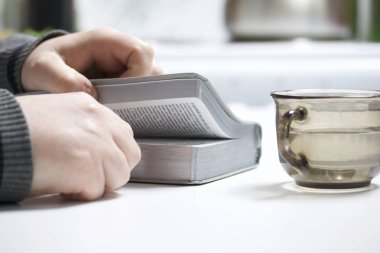 Genç bir adam masada oturan bir gümüş dilim İncil okur. Yanında su ile bir kupa olduğunu.