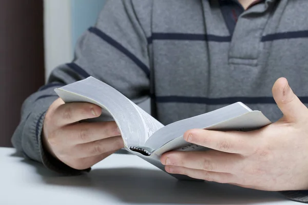 Un joven lee la Biblia con una rebanada de plata sentada a la mesa . — Foto de Stock