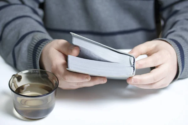 Un joven lee la Biblia con una rebanada de plata sentada a la mesa. Una taza con agua está al lado. . — Foto de Stock