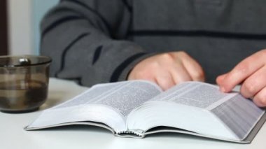 Genç bir adam masada oturan bir gümüş dilim İncil okur. Sonra o kitabı kapatır.