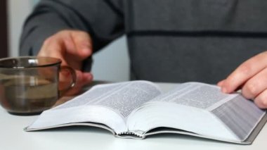 Genç bir adam masada oturan bir gümüş dilim İncil okur. O bardaktan su içer.