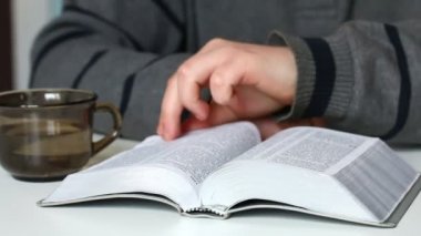 Genç bir adam masada oturan bir gümüş dilim İncil okur. Sayfaları aracılığıyla döndürür.