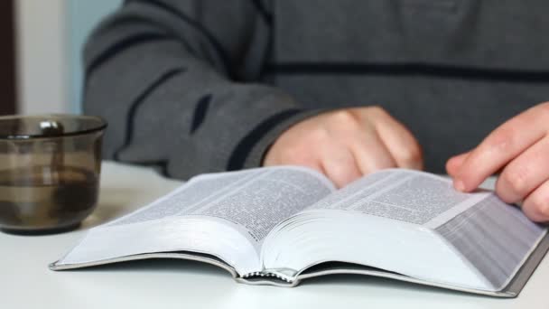一个年轻人坐在桌边看圣经 然后他关上了书 — 图库视频影像