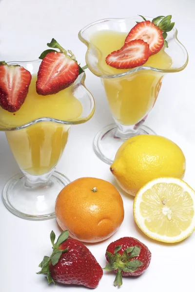 Jelly in de servies, gedecoreerd met aardbeien. Naast de tabel zijn vruchten: mandarijnen, citroen en bayut. — Stockfoto