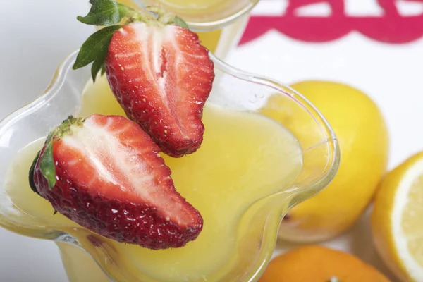 Jelly in de servies, gedecoreerd met aardbeien. Naast de tabel zijn vruchten: mandarijnen, citroen en bayut. — Stockfoto