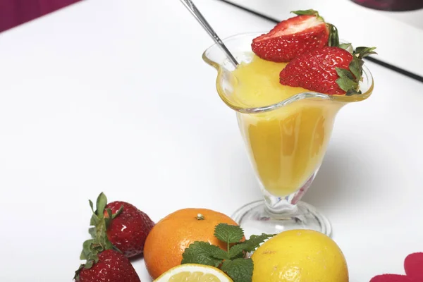 Jelly in de servies, gedecoreerd met aardbeien en munt. Naast de tabel zijn vruchten: mandarijnen, citroen en bayut. — Stockfoto
