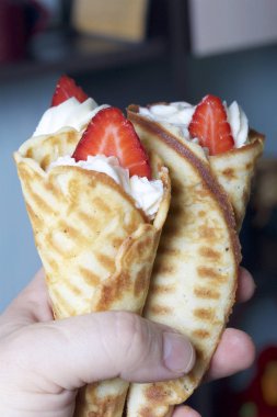 Waffle boynuzları ile krem, çilek ile dekore edilmiştir. Elinde.