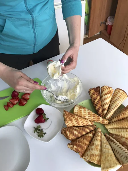 Una mujer pone crema en una bolsa de confitería. Cuernos de gofre con crema, decorados con fresas. Proceso de cocción . —  Fotos de Stock