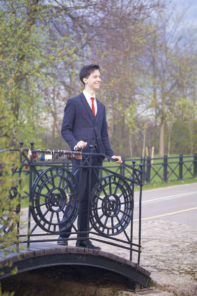 Genç bir adam, Klasik takım elbiseli bir genç. Parkta, vintage köprünün korkuluk ve sevinçle mesafe içine bakarak ellerini koyarak üzerinde duruyor. — Stok fotoğraf