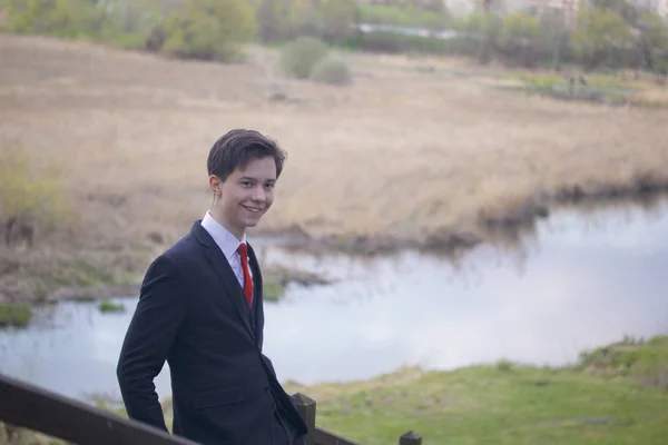 Een jonge man, tiener, in een klassieke pak. Wandelen langs de lanen van het park voorjaarsbijeenkomst. — Stockfoto