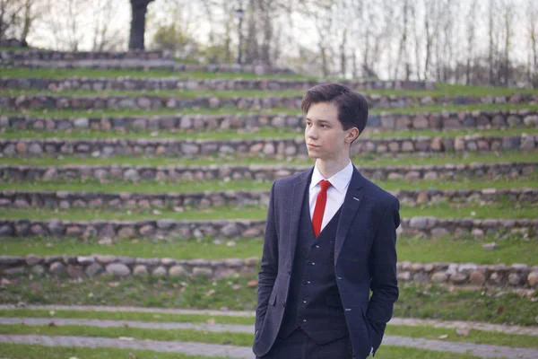 Een jonge man, tiener, in een klassieke pak. Het staat op de stenen trappen van het amfitheater van de zomer, zijn handen in zijn zakken te zetten. — Stockfoto