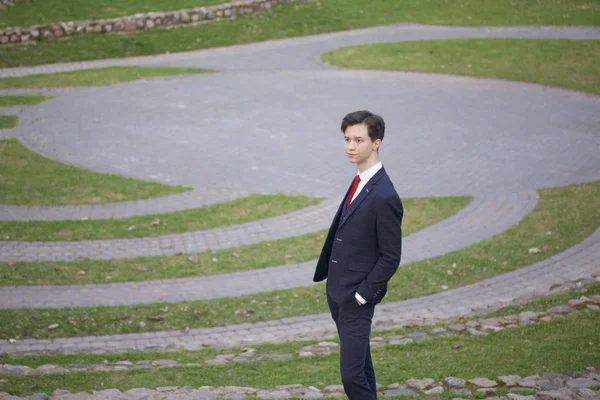 Een jonge man, tiener, in een klassieke pak. Het staat op de stenen trappen van het amfitheater van de zomer, zijn handen in zijn zakken te zetten. — Stockfoto