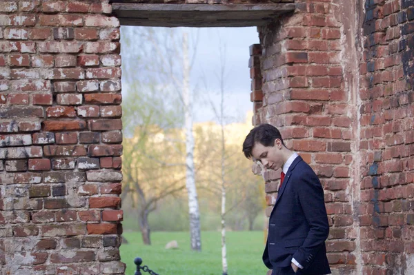 Un jeune homme, un adolescent, en costume classique. La réflexion est debout devant le vieux mur de briques rouges, mettant ses mains dans ses poches . — Photo