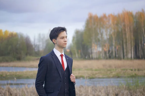 Młody człowiek, nastolatek, w klasycznym garniturze. Spacery wzdłuż alei parku wiosny. — Zdjęcie stockowe