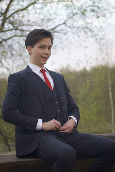 Genç bir adam, bir ergen, klasik bir takım elbiseli. Tezgah üzerinde oturan ceket düğmesini ayarlar. — Stok fotoğraf
