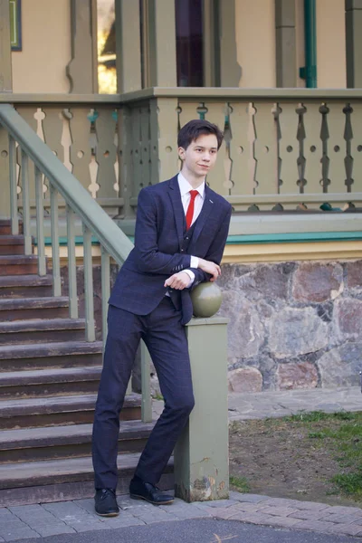 Um jovem, um adolescente, num fato clássico. Ele se levanta, apoiando-se no corrimão de uma escada de madeira . — Fotografia de Stock