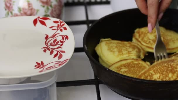 Eine Frau brät Pfannkuchen. verschiebt die fertigen Pfannkuchen von der Pfanne auf den Teller. — Stockvideo