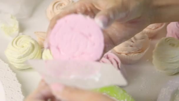 한 여자가 설탕을 뿌리는 장미의 형태로 마시멜로를 굴린다. 테이블의 근처에는 이미 만들어 진 마시멜로가 있습니다. 가까이 서 찍은 사진. — 비디오