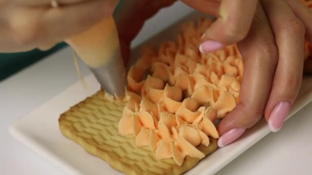 Bir kadın kurabiye ve kremadan hamur işleri hazırlıyor. Kurabiyelere pasta torbasıyla krema sürerName — Stok video