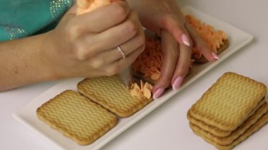 Bir kadın kurabiye ve kremadan hamur işleri hazırlıyor. Kurabiyelere pasta torbasıyla krema sürerName.