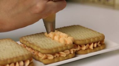 Bir kadın kurabiye ve kremadan hamur işleri hazırlıyor. Pasta poşetindeki kurabiyelere krema sürüyor. Yakın çekim..