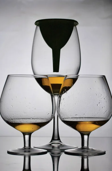 Weinglasbecher auf kurzen Beinen. In der Nähe befindet sich ein Glas auf einem langen Bein, in das ein Trichter eingeführt wird. Sie haben eine kleine Menge Alkohol. — Stockfoto