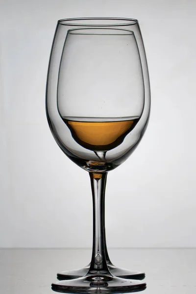 Copos de vidro de vinho em uma perna longa. Ficam um a um. Um deles tem uma pequena quantidade de álcool . — Fotografia de Stock