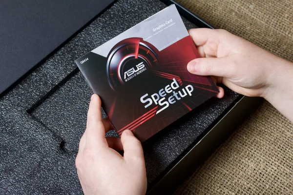 MINSK, BELARUS - 25 NOVEMBRE 2019: Un uomo apre il pacchetto con la scheda grafica ROG Strix GeForce GTX 1660 Ti Advanced Edition 6GB. Il manuale di istruzioni è visibile . — Foto Stock