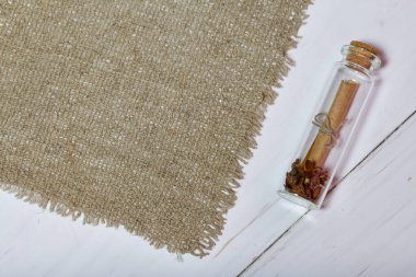 Cam şişedeki not. Keten bir kumaşın yanında. Kumaş beyaz boyalı ahşap tahtalarda yatıyor..