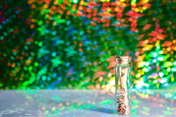 A note folded into a tube lies in a glass bottle. Against the background of rainbow bokeh.