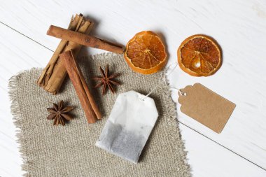 Bir paket çay, anason, tarçın çubukları ve kurutulmuş mandalina dilimleri. Çarşaf parçasının üzerinde yatıyor. Beyaz boyanmış tahtaların arka planına karşı.