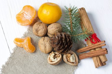 Ceviz, tarçın çubuğu ve çam kozalaklı ladin dalı. Çarşaf parçasının üzerinde yatıyor. Beyaz boyanmış tahtaların arka planına karşı.