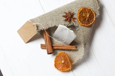 Bir paket çay, anason, tarçın çubukları ve kurutulmuş mandalina dilimleri. Çarşaf parçasının üzerinde yatıyor. Beyaz boyanmış tahtaların arka planına karşı.
