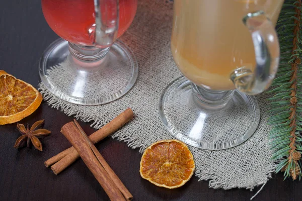 Glasses with a drink of orange and red are on a piece of linen. Slices of dried orange and anise float in them. Nearby are cinnamon sticks and dried oranges and a spruce branch. — Stock Photo, Image