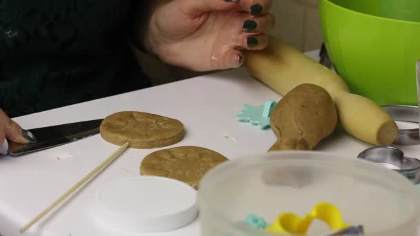 La mujer está preparando galletas de jengibre. Delante de ella hay un cortador de galletas en un palo. Las galletas para hornear se apilan junto a la bandeja para hornear — Vídeos de Stock