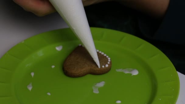 Μια γυναίκα βάζει σταγόνες λευκής ζάχαρης σε ένα μπισκότο από μελόψωμο. Κοντά σε ένα πιάτο είναι μπισκότα με πάγο. — Αρχείο Βίντεο